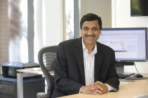 Anant Agarwal sits behind his desk with a computer screen with data behind him.
