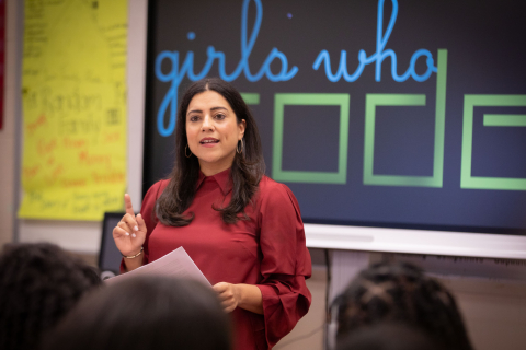 Reshma Saujani speaks to an audience in front of a "Girls Who Code" logo.