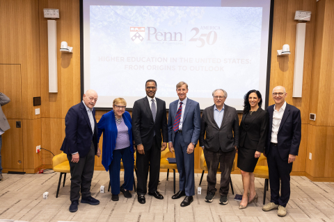 Seven university leaders dressed in suits stand in a line smiling in front of a screen that reads Penn | America 250.